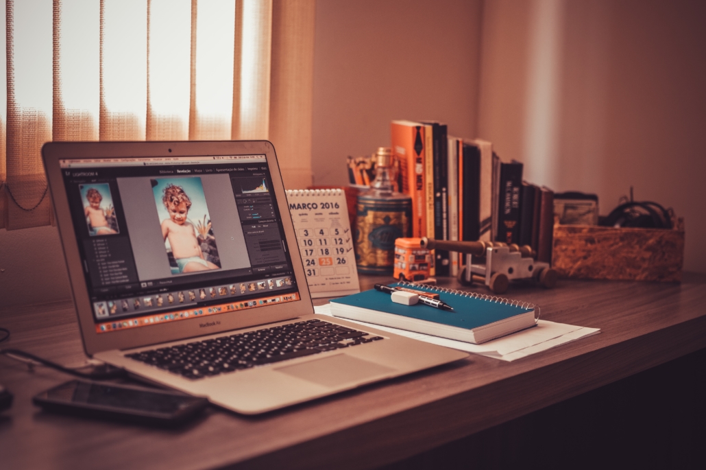 A desktop with office materials, books, and a laptop showing photos of a child in dim lighting