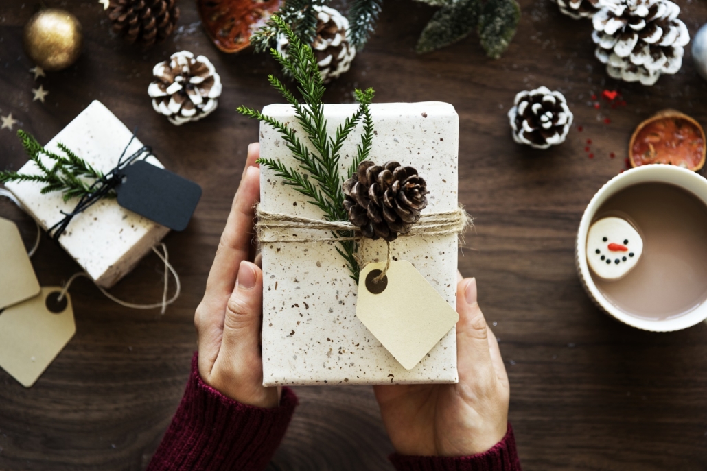 Woman holding a Christmas present in her hands over a table with Christmas decorations and a cup of chocolate