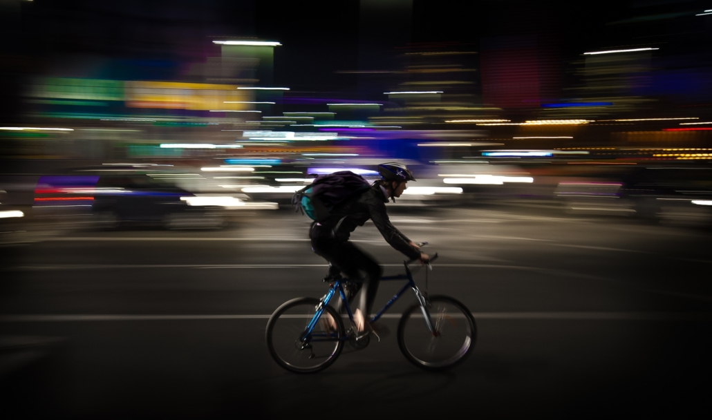 Picture of a courier speeding through the night on his bike through the city