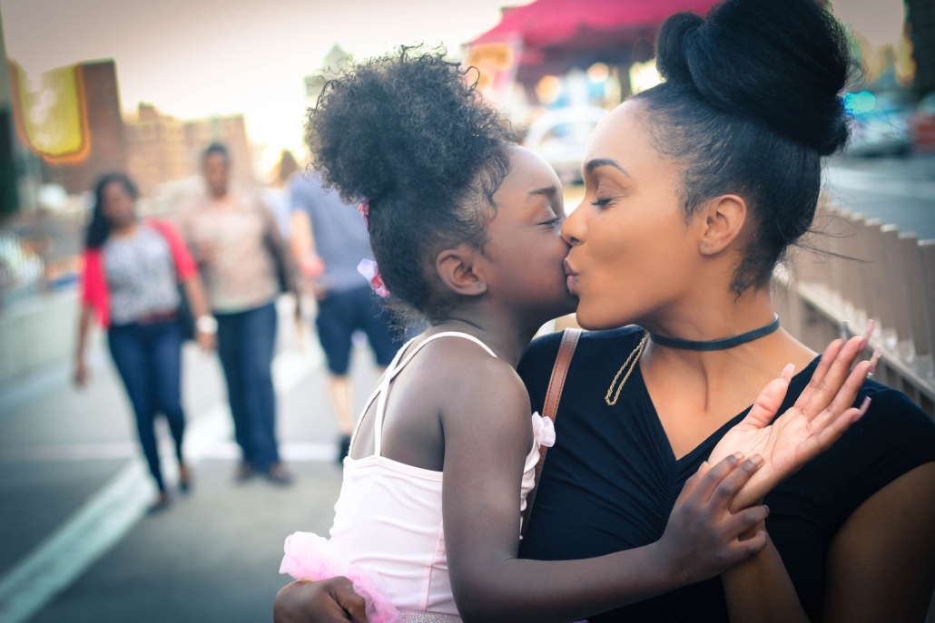 Photo of a mother and daughter giving each other a kiss on a street