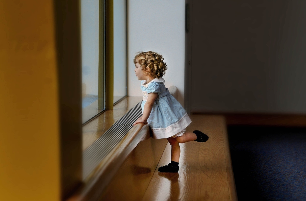 Little girl in a blue dress looking out the window