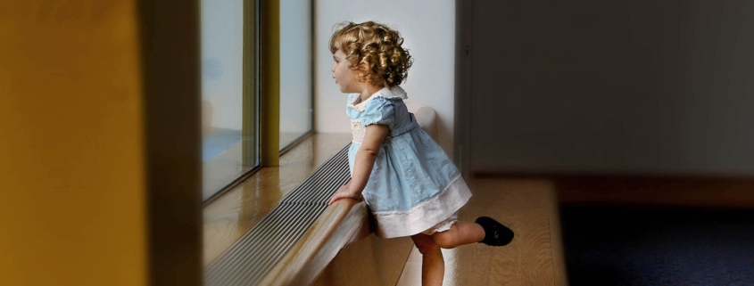 Little girl in a blue dress looking out the window