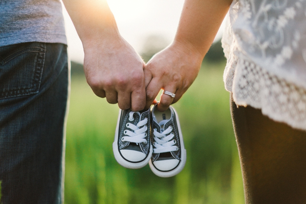 A man and a woman holding hands and a pair of baby shoes photographed from behind