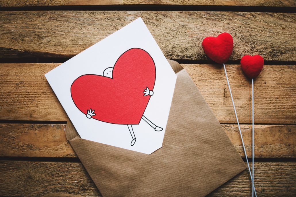 A card showing a figure holding a heart emerging from a brown envelope on a wooden table