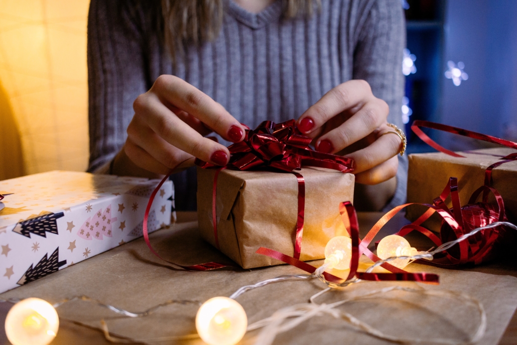 A woman wrapping a gift with a red band on a table with twinkling lights